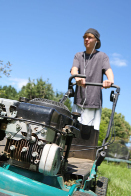 This shows a photo of a teenage boy mowing the lawn. He is wearing headphones.