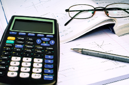 This shows a photo of a graphing calculator beside a math book, a pen, and a pair of glasses.