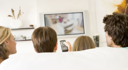 This shows a photo of a family watching a program on a big screen television.