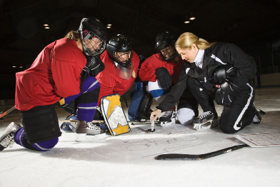 This photo shows three female hockey players listening to instructions from a coach.