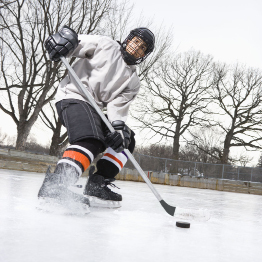 This photo shows a hockey player skating to a stop on an outdoor ice rink.