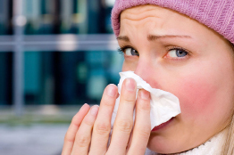 This shows a photo of a young woman with a cold and is holding a tissue to her nose.