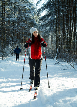 This shows a photo of a young woman cross-country skiing in the forest.