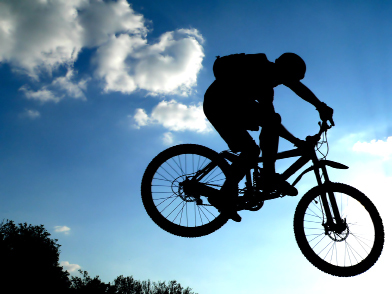 This photo shows the silhouette of a person riding a mountain bike against a blue sky background.