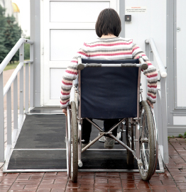 This shows a photo of a woman in a wheelchair who is moving up a ramp towards the door of a house.