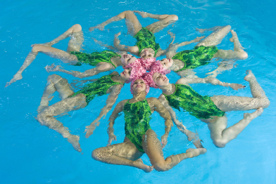 This shows a photo of six synchronized swimmers floating on their backs in a hexagonal formation.
