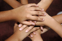 This shows a photo of a circle of many young people’s hands piled on top of each other.
