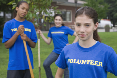 This shows a photo of three youth wearing blue shirts with the word Volunteer across the front. Two of the youths are holding shovels.