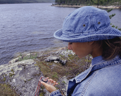 This is a photo of a girl holding a compass while standing at the edge of a lake.