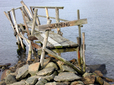 This is a photo of a dock that is falling apart with a warning sign attached to the end of it.
