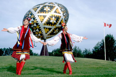 This is a photo of two Ukrainian dancers in front of a giant Easter egg, a roadside attraction, at Vegreville.