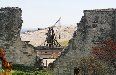 This photo shows a trebuchet in the background and a broken-down stone wall in the foreground.