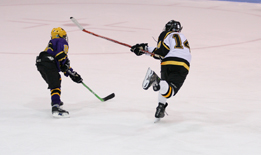 This photograph shows a hockey player shooting the puck while another play attempts to block the shot.