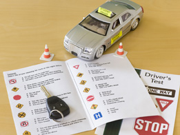This is a photo of a toy car, a car key, and a driver’s licence test.