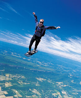 This photo shows a skydiver falling through the air in an upright position with a snowboard on his feet.