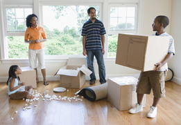 This is a photo of a boy holding a cardboard box and looking at his parents and sister.