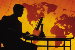 This illustration is of a silhouetted businessman with a computer sitting in front of a world map.