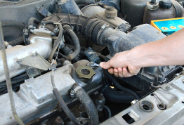 This photo shows someone reaching over a car engine with a wrench in hand.