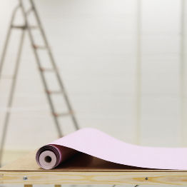 This is a photograph of a roll of wallpaper on a workbench with a ladder in the background
