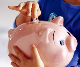 This shows a photo of a child dropping a coin into a piggy bank.
