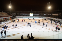 This shows a photo of an outdoor ice rink at night time with many people skating under the lights.
