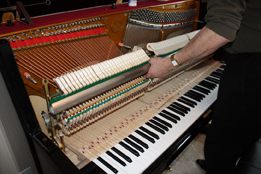 This is a photo of a repairman removing the piano action of an upright piano.