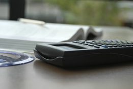 This is a photo of a graphing calculator on a tabletop next to an angle-measuring tool and an open notebook.