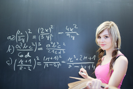 This is a photo of a college-aged woman working on a complex math problem at the blackboard.