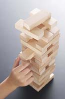 This is a photo of a child’s hand removing a wooden block from a wooden-block tower.