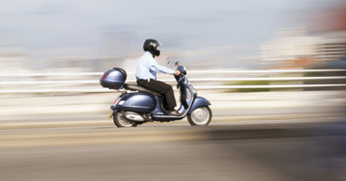 This is an image of a person riding a motor scooter down a stretch of highway.
