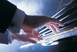 This shows a photo of a man’s hands playing keys on a piano. He appears to be performing on a stage.