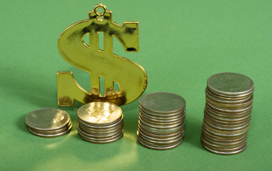 In this photo, stacks of coins are lined up in front of a golden money sign. 