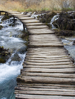 This photo is of a winding wooden bridge over a raging river.