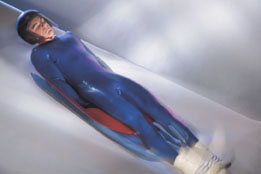 This photo shows a man sliding down a hiil on a luge.