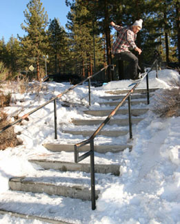 This is a photo of a person doing a snowboarder nose press on the handrail of some stairs covered with snow.