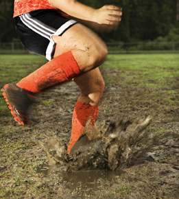 This photo is of a soccer player running through a muddy spot on the pitch.