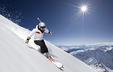 This photo shows a skier coming down a 45 degree slope. There are many snow covered mountains in the background.