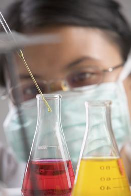 This image shows a worker with two beakers of different coloured liquids. The worker is dropping a reactant into one of the beakers.