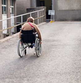In this photo a person in a wheelchair is propelling the  wheelchair up a ramp.
