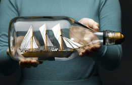 This is a photo of a person holding a bottle containing a model sailing ship.
