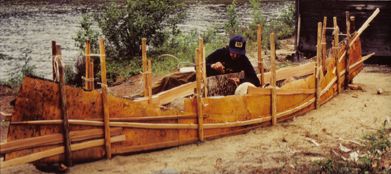 In this photo an artisan is stitching the birch bark on a traditional birch bark canoe.