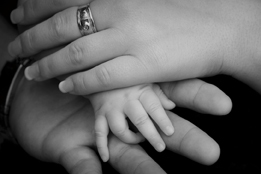 This is a photo of three hands. A mother’s hand on top, a baby’s hand in the middle, and a father’s hand on the bottom.