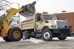 This is a photo of a truck being loaded with snow as a parking lot is being cleared.