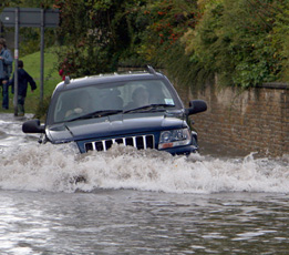 This is a photograph of a SUV driving through a flooded area.
