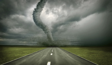 This photograph shows a storm with a tornado at the end of a paved and lined highway.