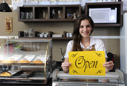 This is a picture of a woman holding an Open sign in a café.