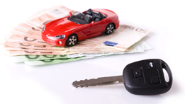 This is a photo of a red toy car on top of some dollar bills with a car key in front.