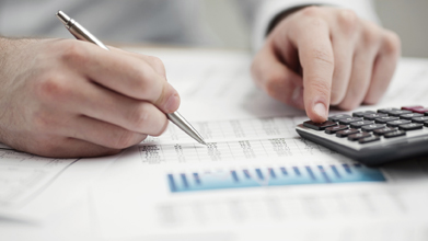 This is a picture of a hand with a pen filling in a form and another hand using a calculator.