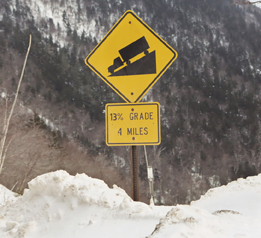 This photograph shows a sign cautioning a steep grade on a mountain.