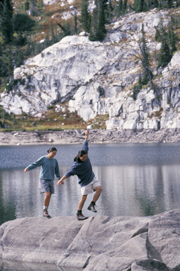 This photograph shows a man and woman balancing on a rock near a river.
